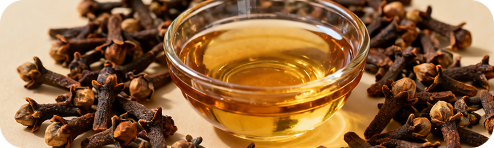 Dried cloves around a bowl of golden oil